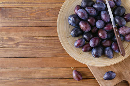 Plate with tasty plums on wooden background