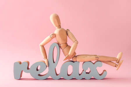 Wooden mannequin with word RELAX on color background