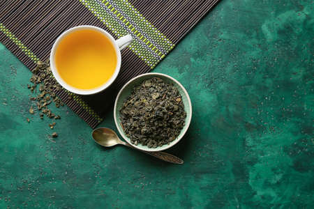 Cup of hot beverage and bowl with dry tea leaves on color backgroundの写真素材