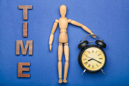 Wooden mannequin with word TIME and alarm clock on color backgroundの写真素材