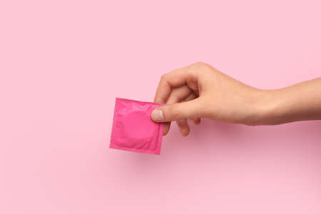 Female hand with wrapped condom on color backgroundの写真素材