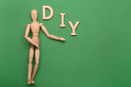 Wooden mannequin with word DIY on color background