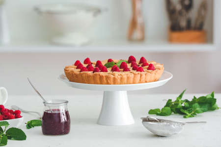 Dessert stand with tasty raspberry pie and jam on table in kitchenの写真素材