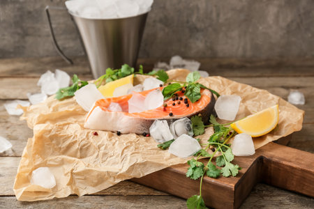 Raw salmon steak, ice cubes and herbs on tableの写真素材