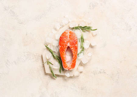 Raw salmon steak and ice cubes on light background