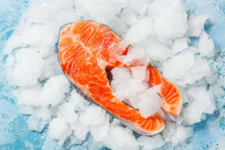 Raw salmon steak and ice on color backgroundの写真素材