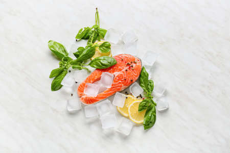 Raw salmon steak, lemon and ice cubes on light background