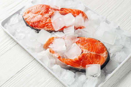 Raw salmon steaks and ice cubes on light background