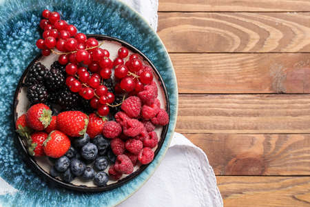 Plate with different tasty berries on wooden tableの写真素材