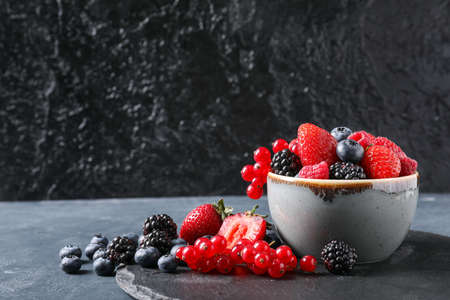 Bowl with different ripe berries on dark background