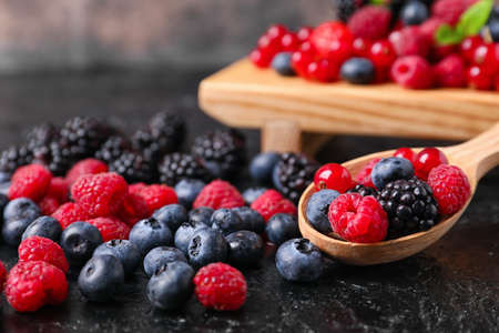 Spoon and tray with different tasty berries on dark background