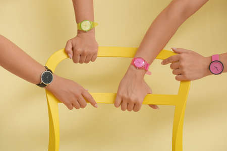 Female hands with wrist watches holding chair near color wallの写真素材