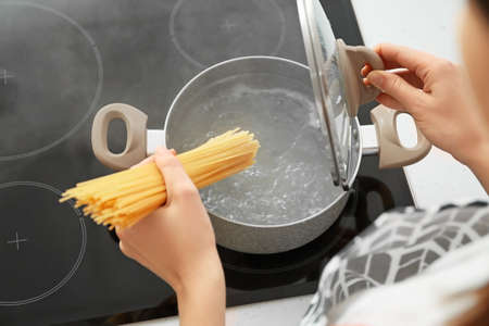 Woman cooking tasty pasta in kitchen