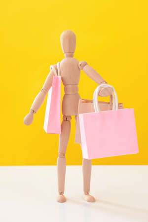 Wooden mannequin with shopping bags on color backgroundの写真素材