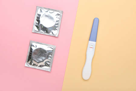 Wrapped condoms and pregnancy test on color background