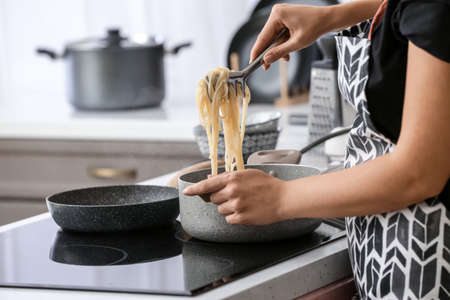 Woman cooking tasty pasta in kitchenの写真素材