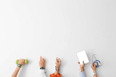 Hands with wrist watches, dumbbell, tablet computer and stethoscope on light backgroundの写真素材