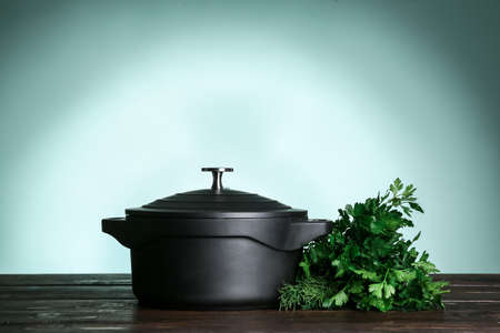 Cooking pot and parsley on table against color background