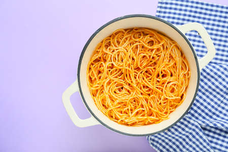 Cooking pot with pasta on color background