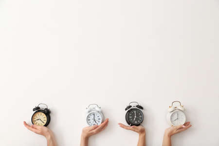 Female hands with alarm clocks on light backgroundの写真素材
