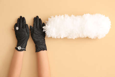 Female hands in rubber gloves, ring and wrist watch with dust brush on color backgroundの写真素材