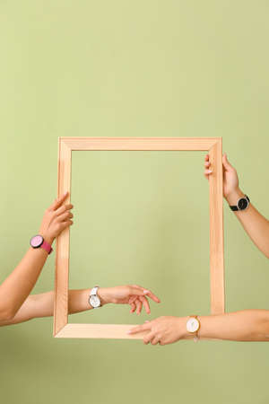 Female hands with wrist watches holding wooden frame on color background