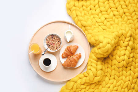 Tray with tasty breakfast and knitted plaid on white background