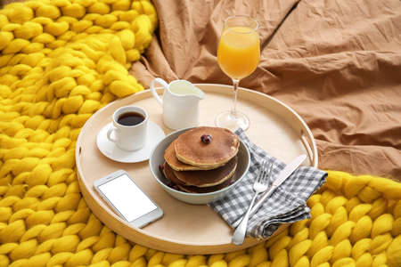 Tray with tasty breakfast and mobile phone on bedの写真素材