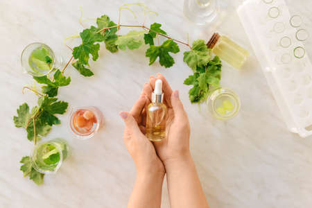 Female hands with bottle of grape seed oil and laboratory flasks on white backgroundの写真素材