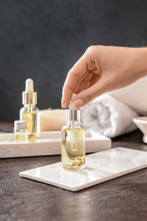 Female hand with bottle of grape seed oil on dark background