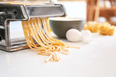 Pasta maker with dough on table in kitchenの写真素材