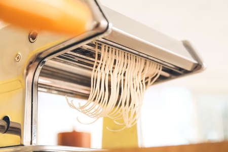 Pasta maker with dough on table in kitchen
