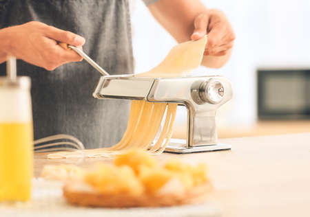 Man making pasta with machine on table in kitchenの写真素材