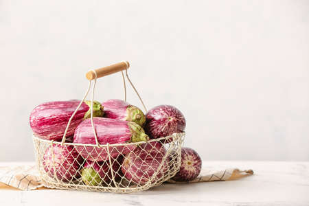 Basket with fresh eggplants on light background