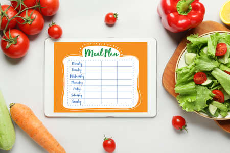 Healthy vegetables and tablet computer with diet plan on screen against light backgroundの写真素材