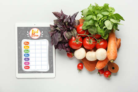 Healthy vegetables and tablet computer with diet plan on screen against light backgroundの写真素材
