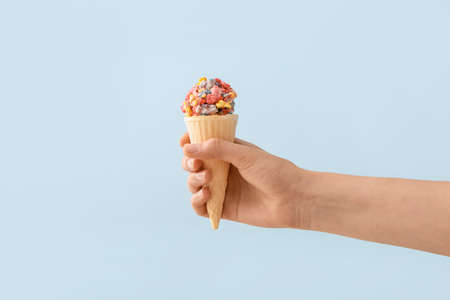Woman holding waffle cone with popcorn ball on color background