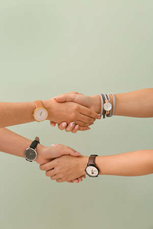 Women with watches shaking hands on color backgroundの写真素材
