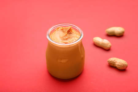 Jar of tasty peanut butter on color background