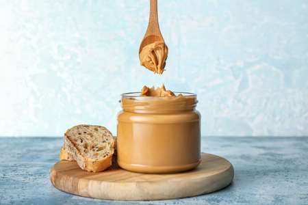 Jar with tasty peanut butter and sliced bread on table