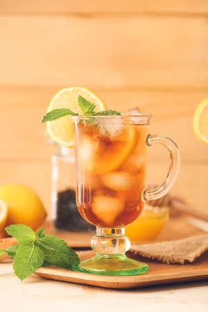 Cup of cold black tea with lemon on light wooden background
