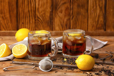 Cups of cold black tea with lemon on wooden backgroundの写真素材