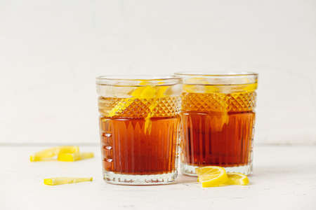 Glasses of cold black tea with lemon on light background