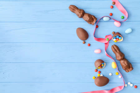 Tasty chocolate Easter bunnies and eggs with candies on color wooden background