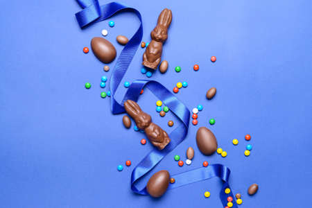 Tasty chocolate Easter bunnies and eggs with candies on color backgroundの素材 [FY310172511257]