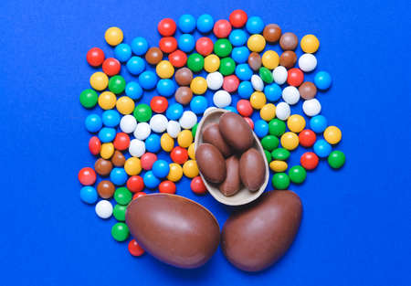 Tasty chocolate eggs and candies on color background