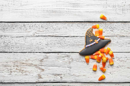 Tasty candy corns and cookie for Halloween on white wooden background