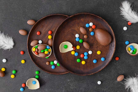 Plates with tasty chocolate eggs and candies on dark background