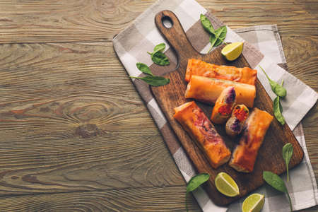 Board with tasty fried spring rolls on wooden background
