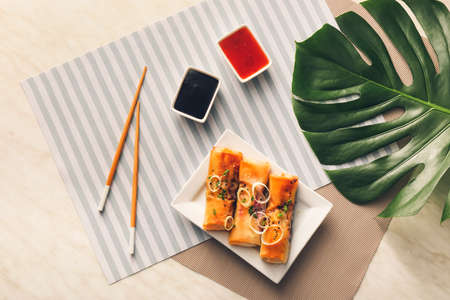 Plate with tasty fried spring rolls and sauces on light background